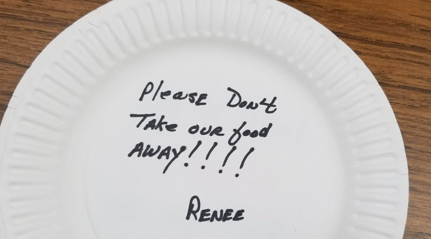 A message written on a paper plate that reads, 'please don't take our food away!', written by a Meals on Wheels recipient