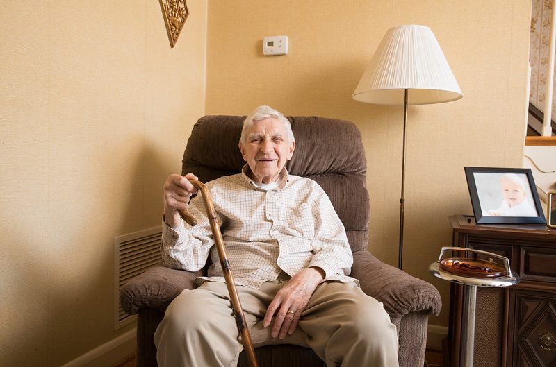 Smiling elderly with cane sitting in armchair at home