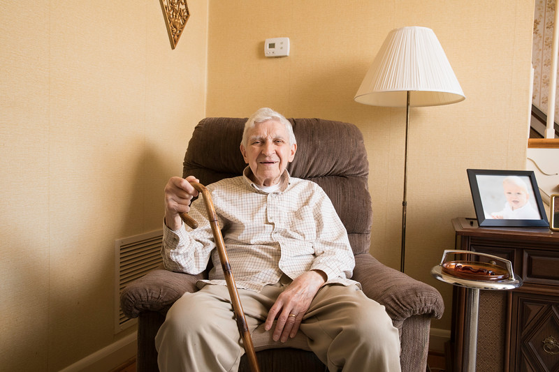 Smiling elderly with cane sitting in armchair at home