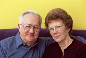 Smiling older couple with glasses sitting on couch